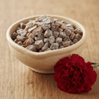 A warm, cream-colored ceramic bowl of handcrafted Carnation incense, resting on an aged oak surface next to a deep-red carnation bloom.