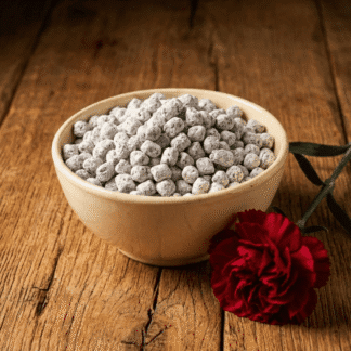 A cream-colored ceramic bowl of handcrafted Carnation incense, resting on an oak surface next to a deep red carnation bloom.